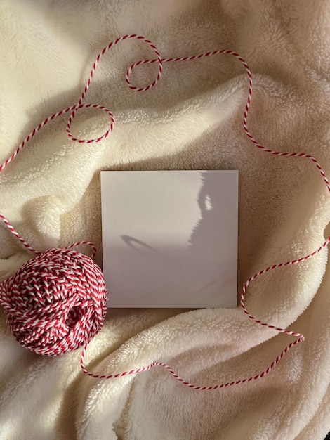 A red and white thread for tied Christmas gifts lies next to a white square on a fur background in the rays of the sun Copy space Top view Flatlay