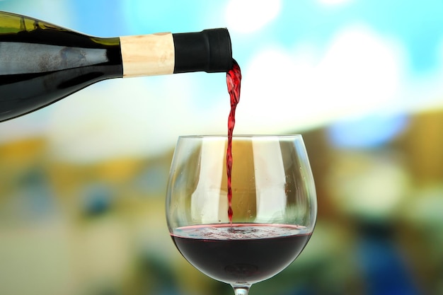 Red wine being poured into wine glass on bright background