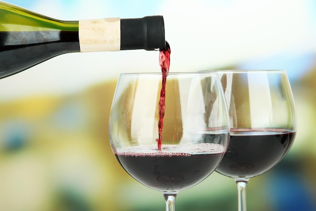 Red wine being poured into wine glass on bright background