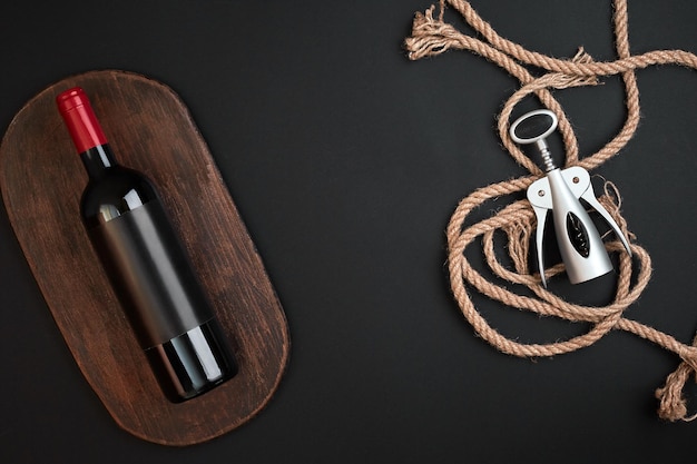 Red wine bottle and corkscrew on black background top view with copy space