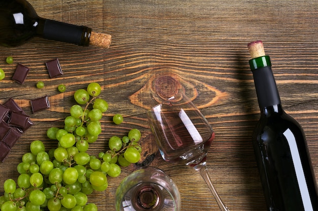 Red wine bottle, grape, chocolate and glasses over wooden table. Top view with copy space. Still life. Flat lay