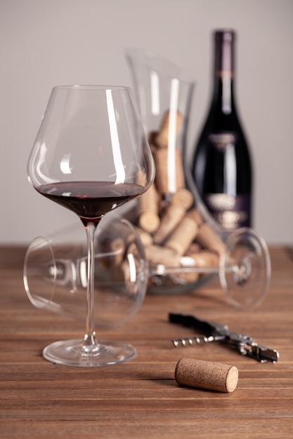 red wine glass, bottle, corkscrew, decanter, corks on wooden table