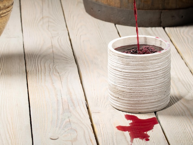 Red wine is poured from an earthen jug into a glass on the table