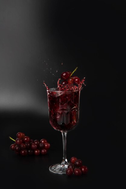 Red wine is poured into a wine glass on a black background with grapes and splash