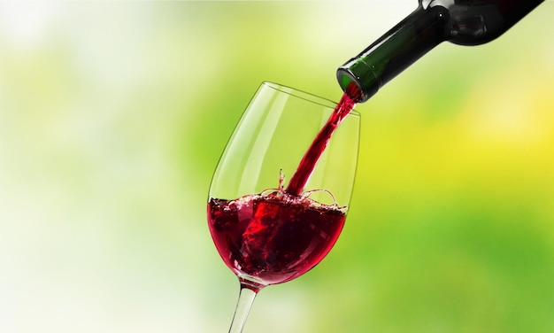 Red wine pouring in glass on green, close-up view