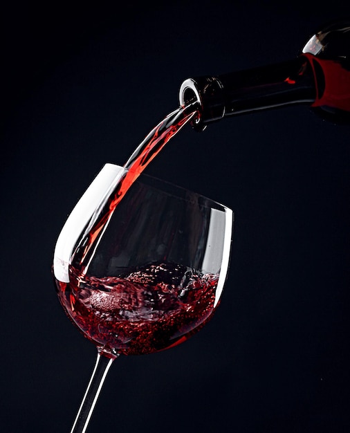 Red wine pouring into wine glass on black background