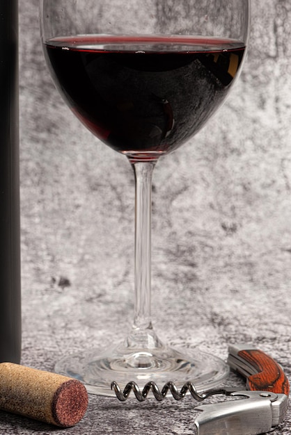 Red wine served in a crystal glass with a bottle beside it and corkscrew