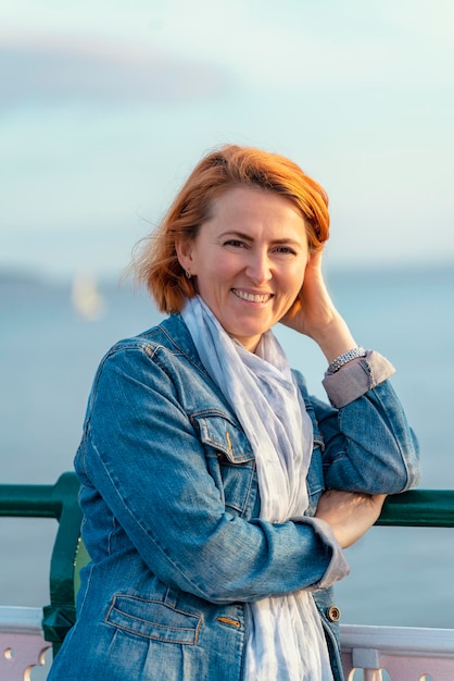 Red womanl in blue dress and jeans jacket resting on the seashore at sunset