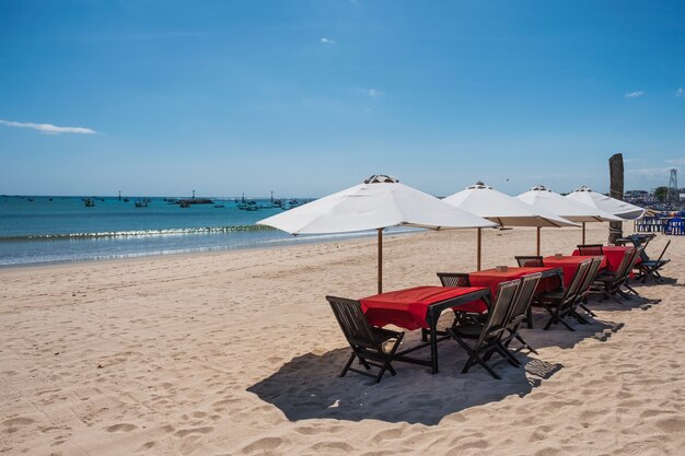 Red wooden dining table with white umbrella on the beach