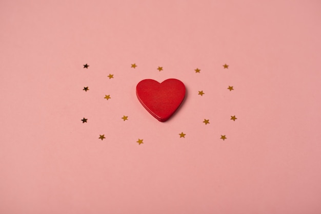 Red wooden heart and little golden stars on the rose background