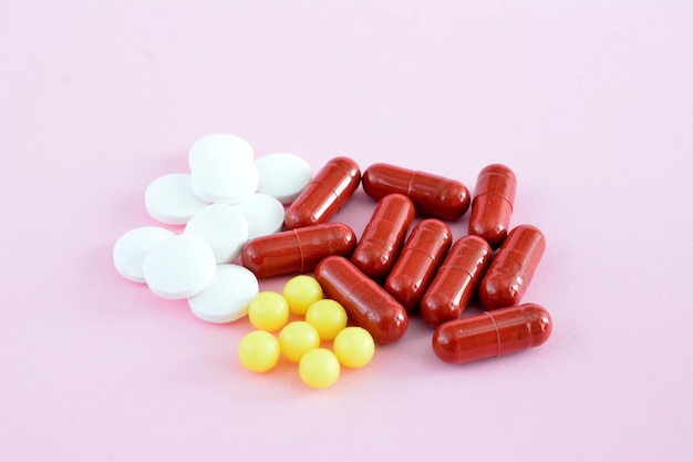 Red and yellow pills and capsules on a pink background isolated closeup