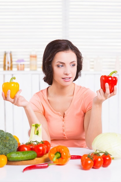 Red or yellow? Thoughtful young woman holding colorful peppers in hands and choosing the one