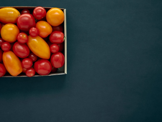 Red and yellow tomatoes in a cardboard box on a dark background with copy space