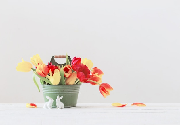 Red and yellow tulips in bucket and ceramic rabbit on white background