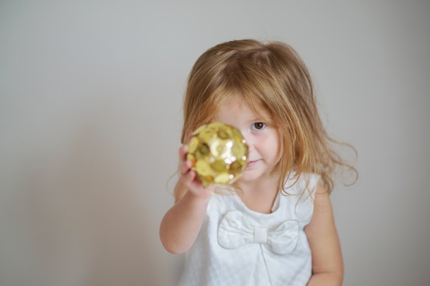 Redhair girl with gold ball ornament on light gray wall