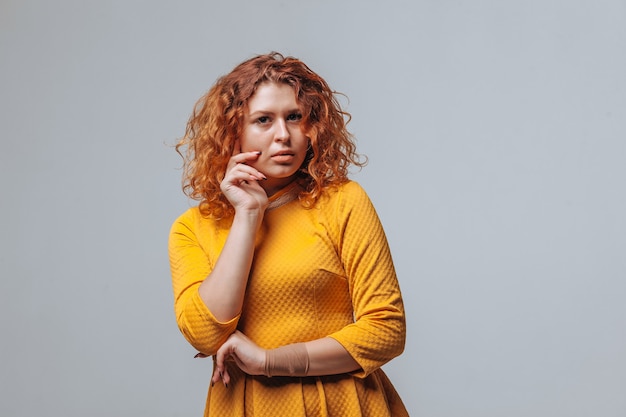 Redhaired curly girl Thinks on a light gray background