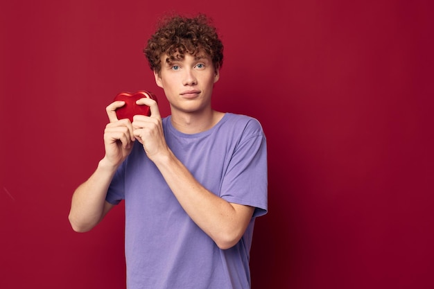 Redhaired curly guy a box in the form of a heart in his hands red background