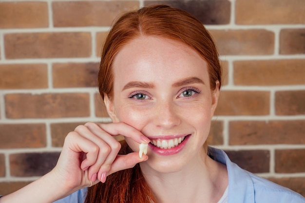 Redhaired ginger female with snowwhite smile holding white wisdom tooth after surgery removal of a tooth