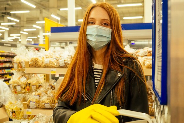 Redhaired ginger woman in casual black leather jacket rubber gloves yellow use antibacterial gel in empty super market second wave