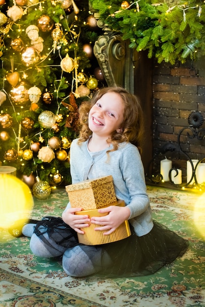 Redhaired girl opens a gift near the Christmas tree