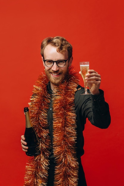 Redhaired handsome man in glasses and a golden boa raises a glass of champagne Celebration of the new year