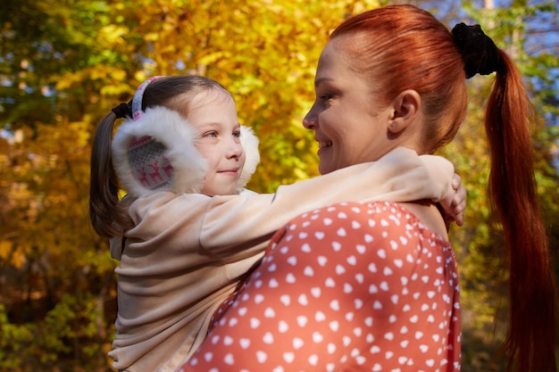 A redhaired happy woman with a little daughter in her arms in an autumn sunny park