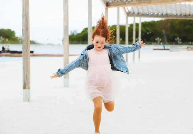 Redhaired little girl runs on the sand on the city swimhappy child on the beach