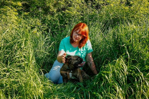 Redhaired owner with a french bulldog sitting among the tall grass hiding from the sun on a summer day