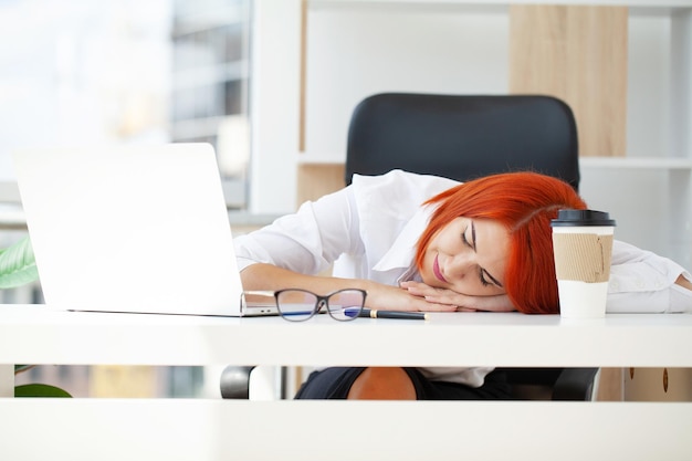 Redhaired tired cute beautiful business woman sit indoors in office using laptop computer