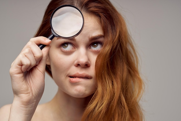 Redhaired woman magnifier near the face hygiene closeup