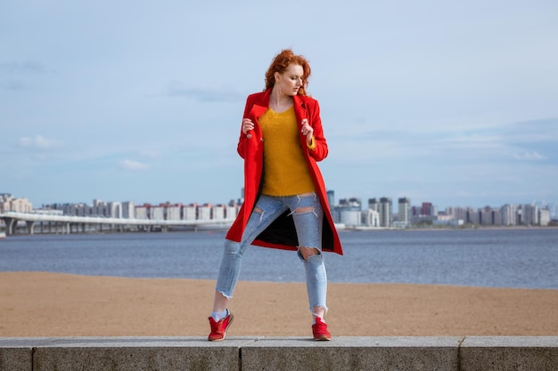 Redhaired woman poses against river in city with buildings in background