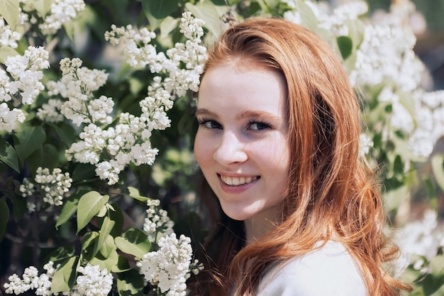 Redhaired young girl on the background of a white flowering bush in summer