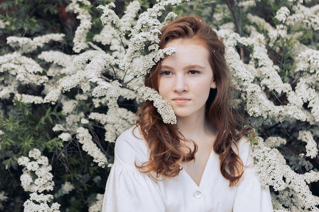 Redhaired young girl on the background of a white flowering bush in summer