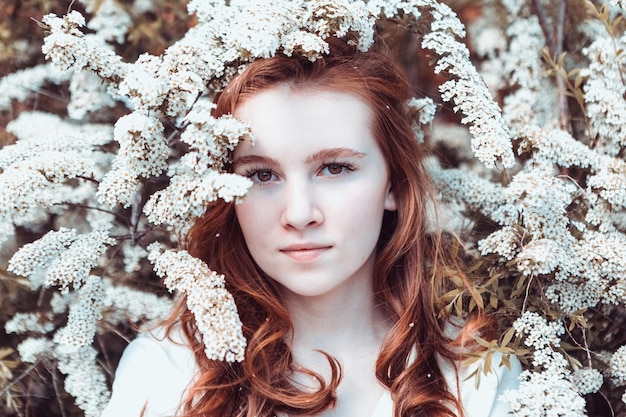 Redhaired young girl on the background of a white flowering bush in summer