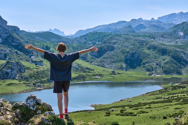 Redhaired young girl with short hair standing with open arms looking into a mountain lake