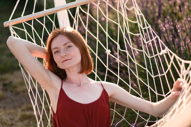 A redhaired young girl without makeup is resting on a hammock in a lavender field Summer vacation and travel time