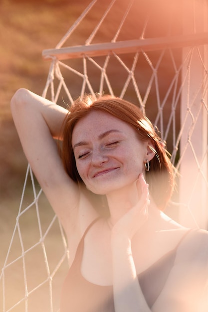 A redhaired young girl without makeup is resting on a hammock in a lavender field Summer vacation and travel time