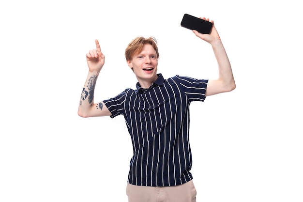 Redhaired young man in a blue tshirt on a white background with a mobile phone in his hands