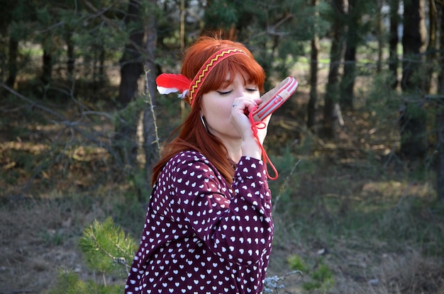 Redhaired young woman with feathers in her hair drinks water from a wineskin