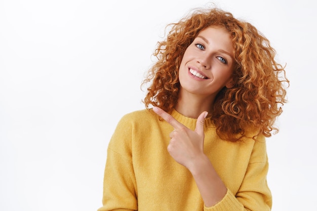 redhead caucasian woman with curly hair, wear winter yellow sweater, pointing at left