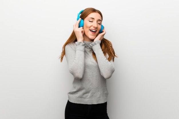 Redhead girl over white wall listening to music with headphones