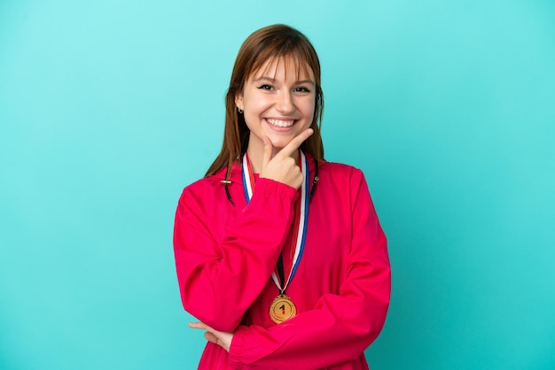 Redhead girl with medals isolated o blue background smiling