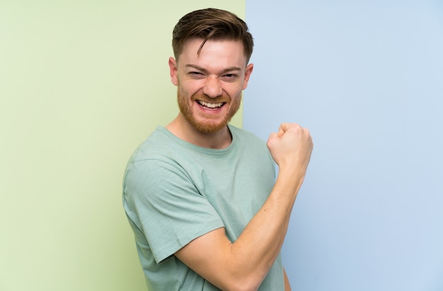 Redhead man over colorful wall celebrating a victory