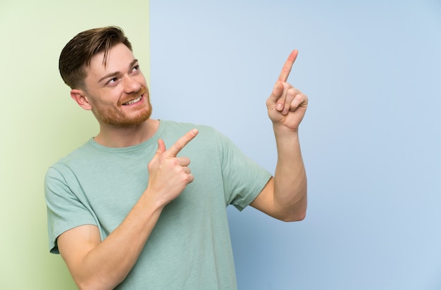 Redhead man over colorful wall pointing with the index finger a great idea