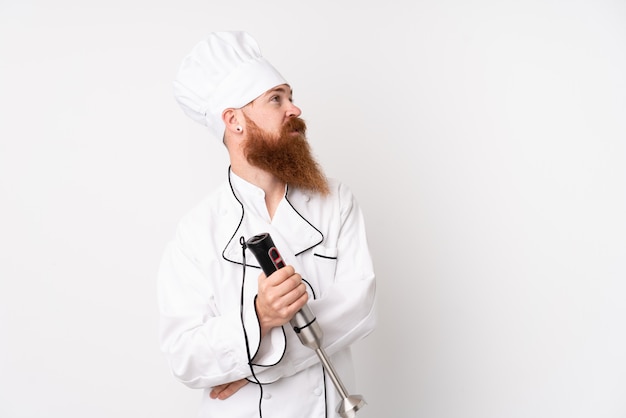 Redhead man using hand blender over isolated white wall laughing