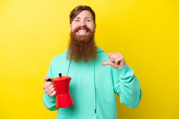 Redhead man with beard holding coffee pot isolated on yellow background proud and selfsatisfied