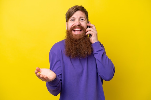 Redhead man with beard isolated on yellow background keeping a conversation with the mobile phone with someone