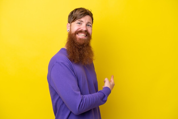 Redhead man with beard isolated on yellow background pointing back