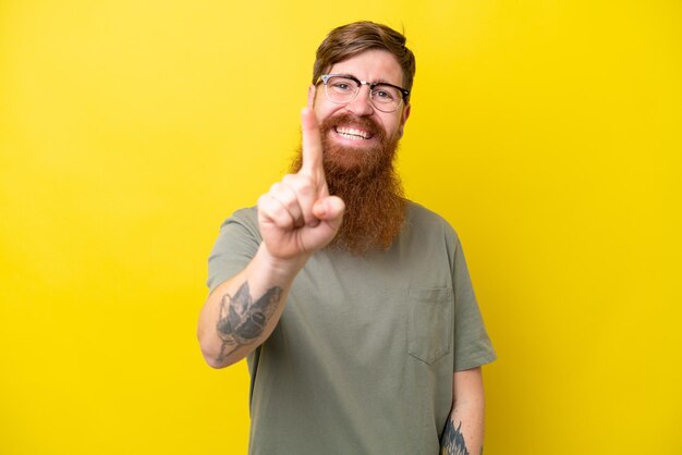 Redhead man with beard isolated on yellow background smiling and showing victory sign