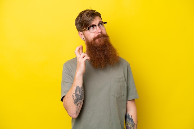 Redhead man with beard isolated on yellow background with fingers crossing and wishing the best